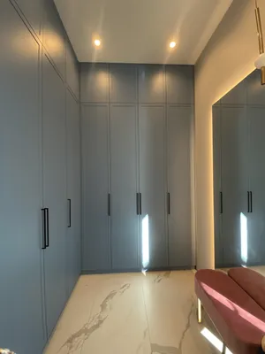 Высокий встроенный шкаф из крашеного МДФ с тонкими черными ручками и антресолями в интерьере прихожей с мраморным полом.